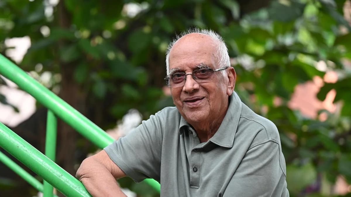 A black-and-white portrait of Singeetham Srinivasa Rao, aged, with a calm expression, wearing a white shirt and glasses.