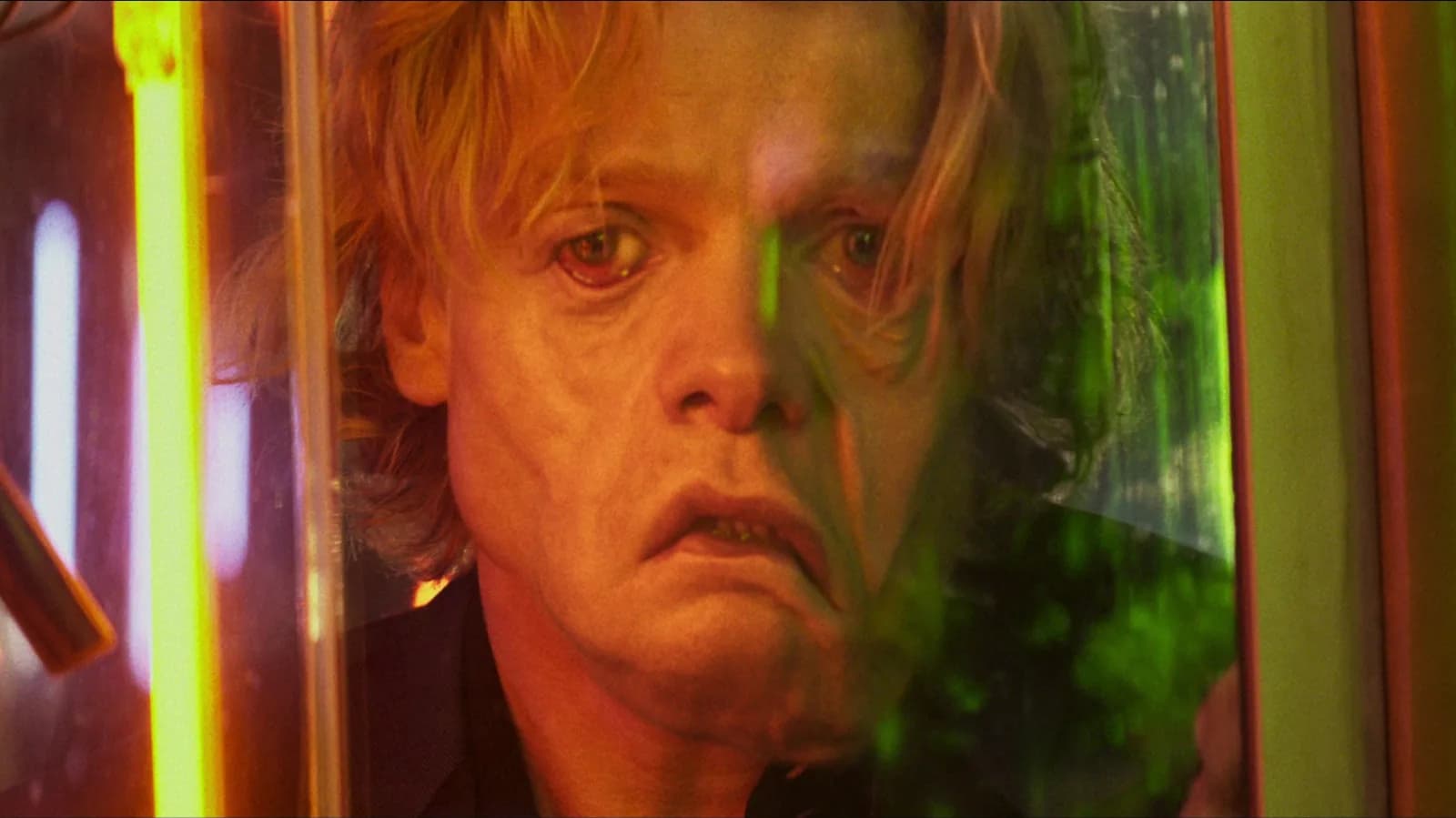 A close-up of a man's face slowly crumbling into clay, eyes wide, mouth open mid-scream. The skin peels away like wet plaster.