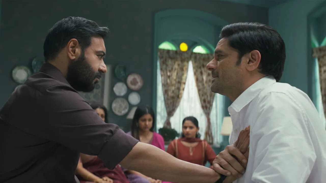 Ajay Devgn in a tense scene from Drishyam: The Conclusion, standing in shadow, eyes sharp.