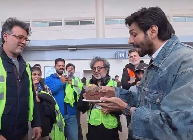 Kartik Aaryan holding a cake on the Captain India set in London after receiving the National Award